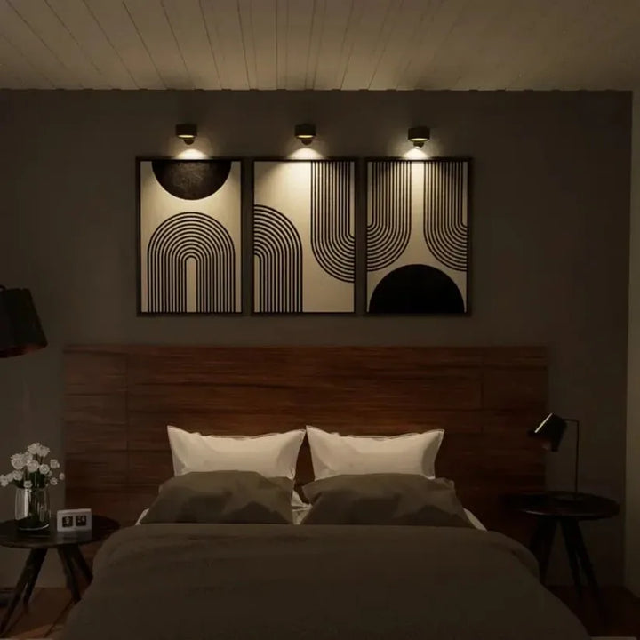 Tre sorte væglamper oplyser hver sin grafiske plakat over en seng i et mørkt soveværelse 10