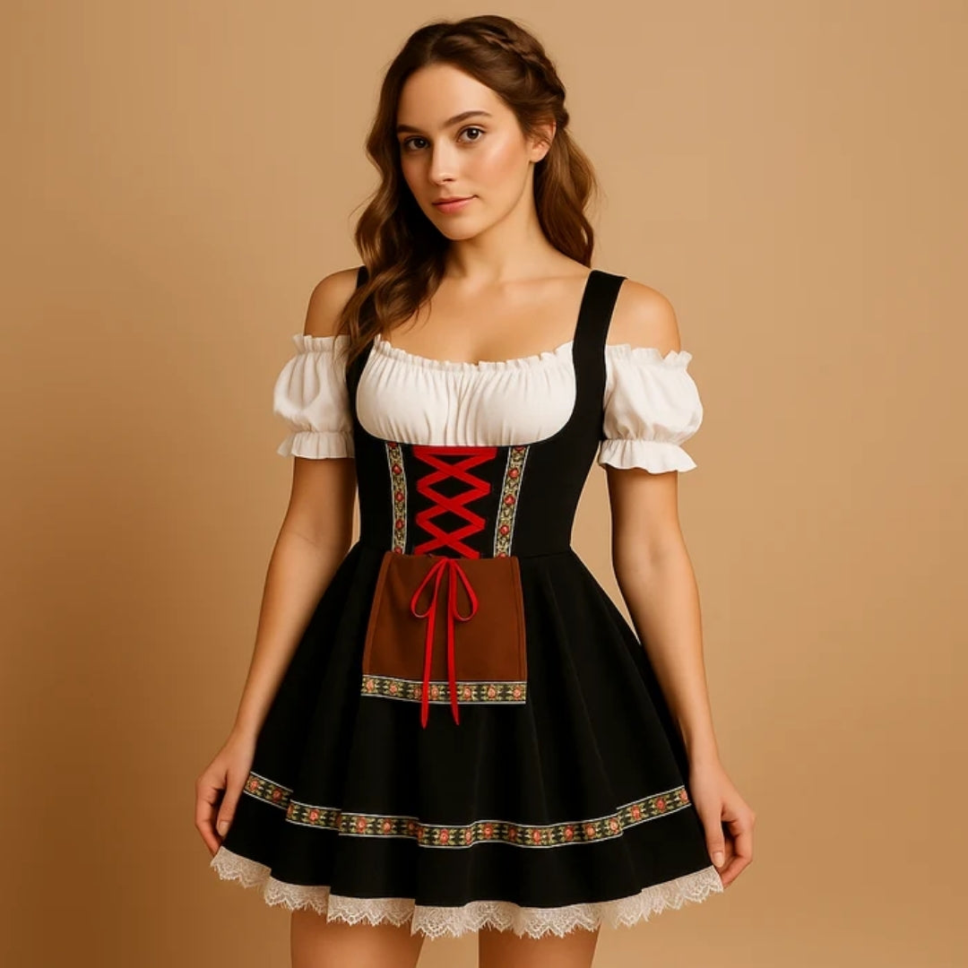 Model i sort dirndl med rød snøring, brunt forklæde med bånd, blomsterbort og hvid blondekant, set let fra siden. 7