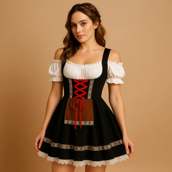 Model i sort dirndl med rød snøring, brunt forklæde med bånd, blomsterbort og hvid blondekant, set let fra siden. 7