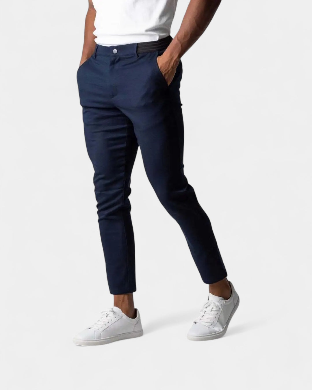 Model i marineblå smalle bukser med elastisk linning, hvid t-shirt og hvide sneakers, hænder i lommerne 2