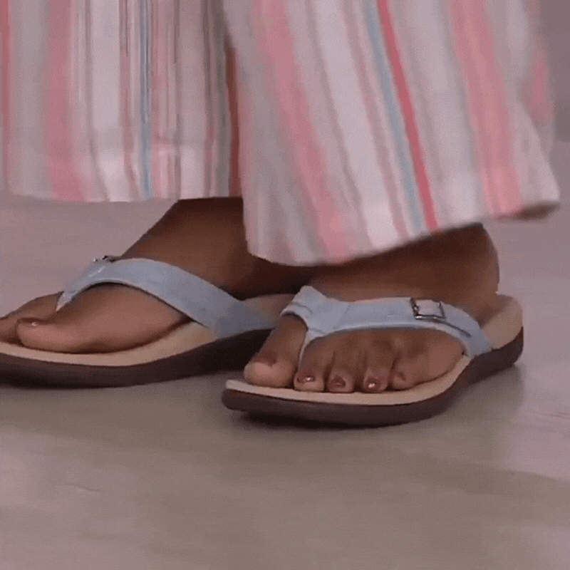 Fødder i lyseblå sandaler med spænde og beige sål, set under stribet buksebenet 16