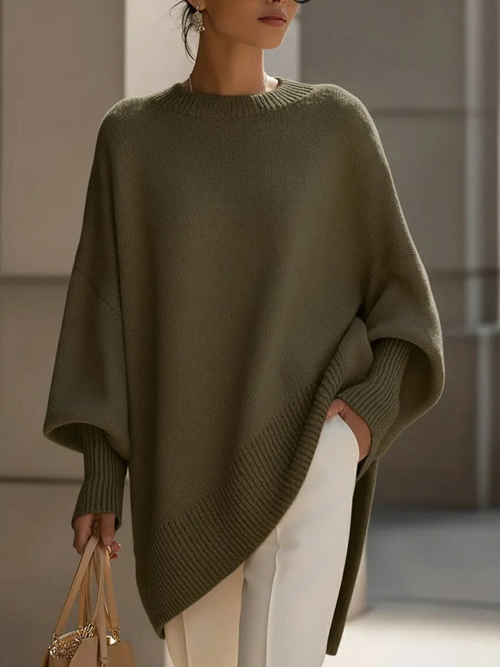 Model i olivengrøn oversize strikbluse med ribkant og ribstrikkede ærmeopslag, hvide bukser og taske. 7