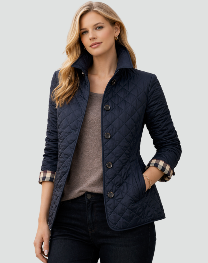 Model i marineblå quiltet jakke med opstående krave over brun trøje og mørke jeans, med ternet foer i ærmerne. 5