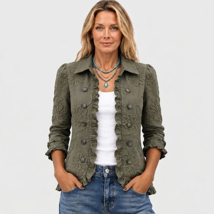 Modellen set forfra i den olivengrønne jakke med åben front, flæsekant og blomsterbroderi, båret med hvid top, turkis halskæde og jeans. 2