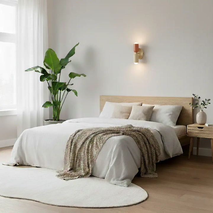 Tændt væglampe i terracotta og creme over en seng med hvidt sengetøj og trægavl, med stor grøn plante og rund lys tæppe. 8