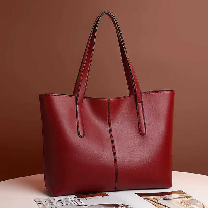 Rød totebag med lange stropper stillet på et hvidt bord med blade foran 3