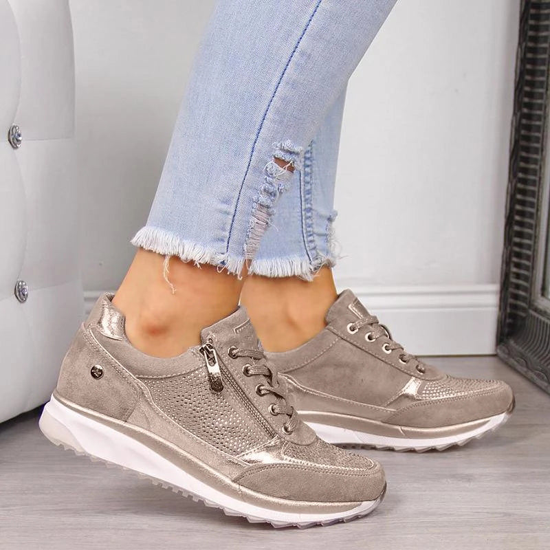 Model i lyse jeans med flossede flænger bærer beige snøresko med lynlås på siden, perforeret overdel og hvid sål. 1