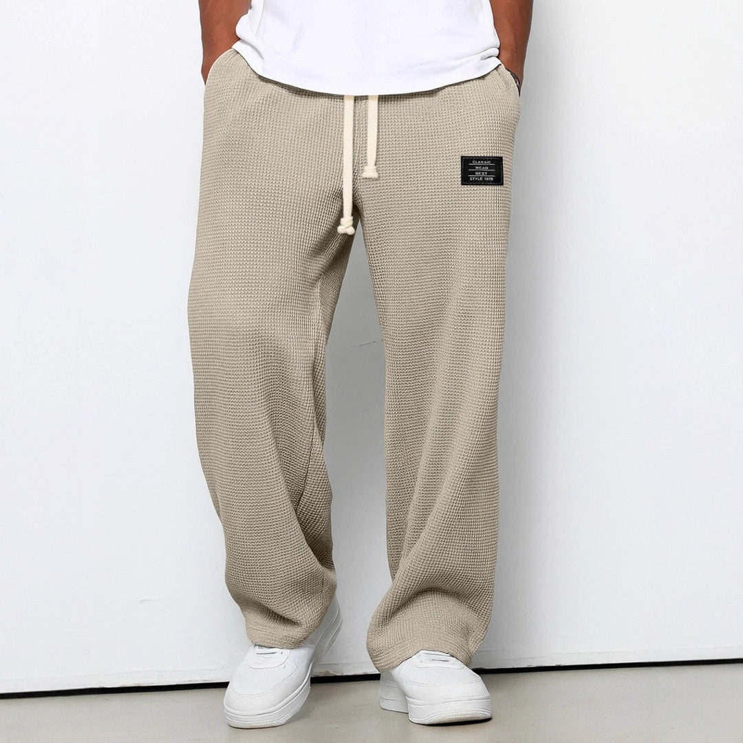 Beige vaffelstrikbukser med vide ben og snøre i taljen, set forfra på en model med hvide sneakers. 6
