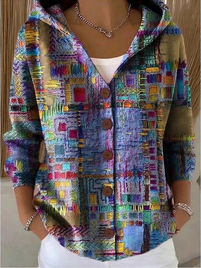 Model i knappet hættetrøje med farverigt patchwork-mønster af syede felter i blå, lilla, grøn og orange, hænder i lommerne. 1