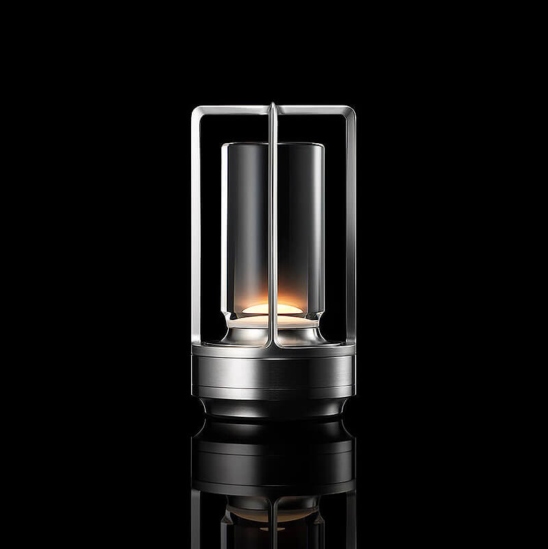 Lampe med sølvfarvet metalstel og klar glasskærm, tændt mod sort baggrund med spejling. 10