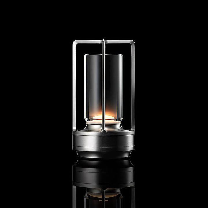 Lampe med sølvfarvet metalstel og klar glasskærm, tændt mod sort baggrund med spejling. 10