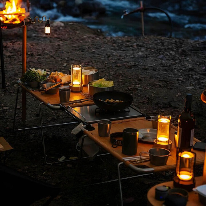 Tændte lamper på bordene ved en udendørs campingplads om aftenen, ved siden af gryder, kopper og mad. 4