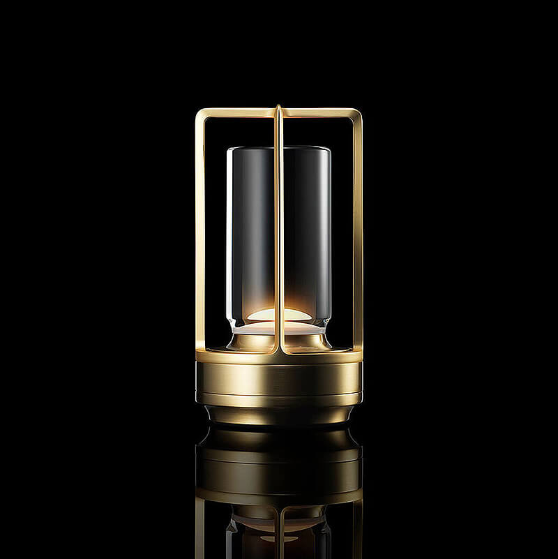 Lampe med messingfarvet metalstel og klar cylindrisk glasskærm, tændt mod sort baggrund med spejling i underlaget. 1