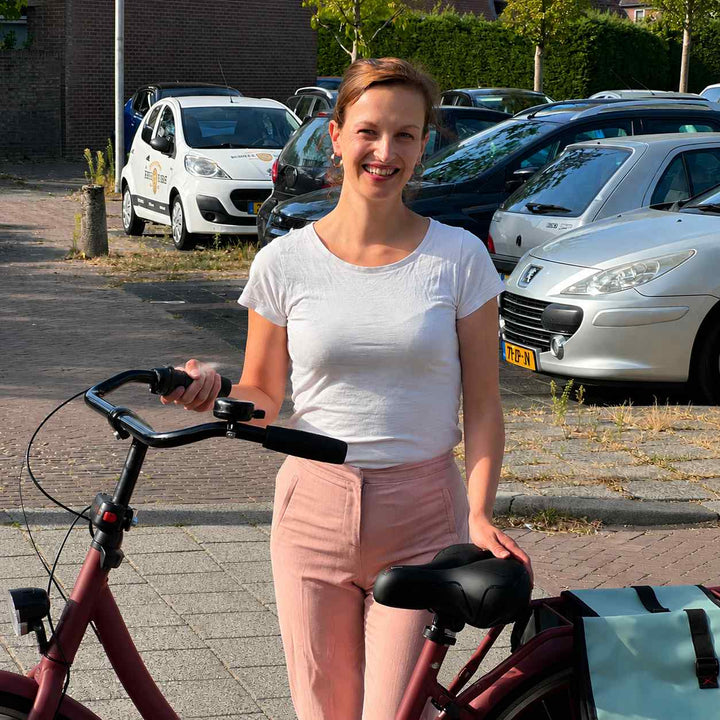 Smilende kvinde står ved en rød cykel med den sorte brede sadel, og lægger hånden på sædet. 7