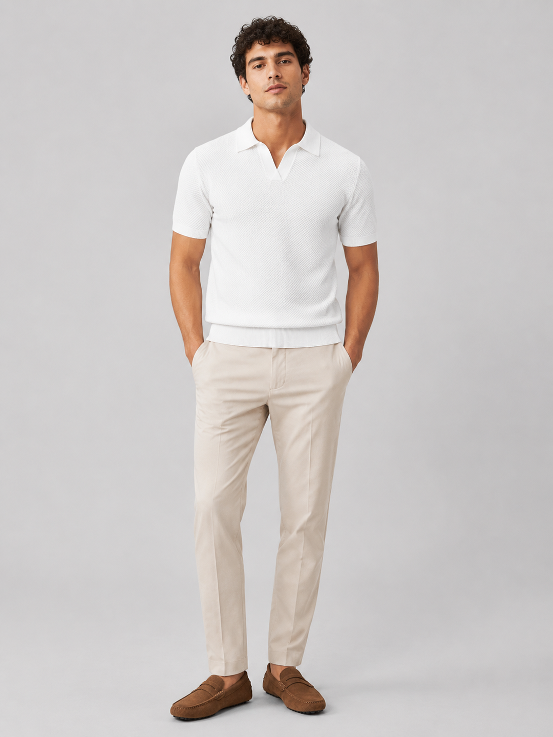 Helfigur af model i hvid strikpolo med beige bukser og brune ruskindsloafers, set forfra 32