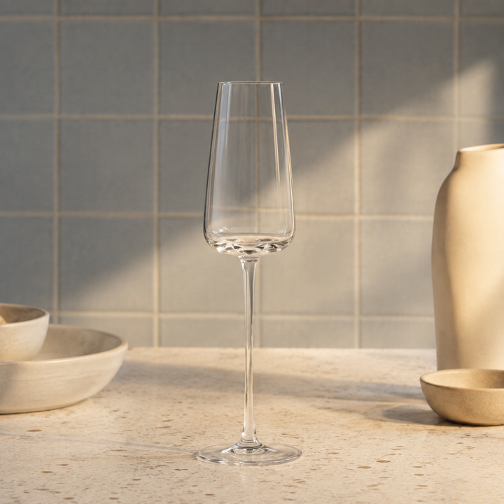 Tomt smalt champagneglas med lang stilk på en bordplade foran blågrå fliser med keramikskåle ved siden af. 14
