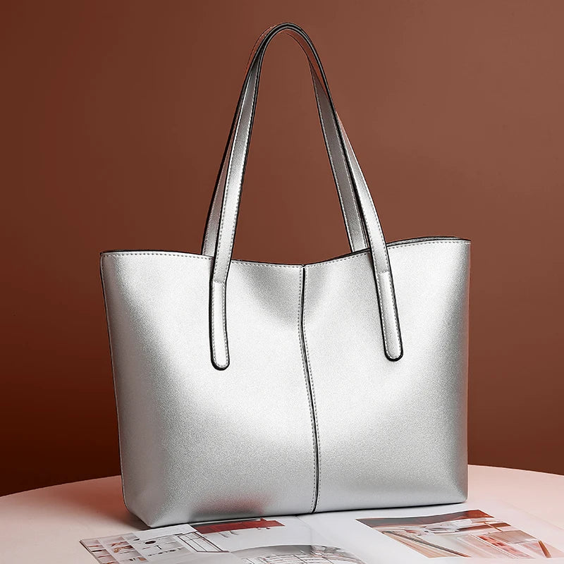 Sølvfarvet totebag med lange stropper stillet på et hvidt bord foran brun væg 2