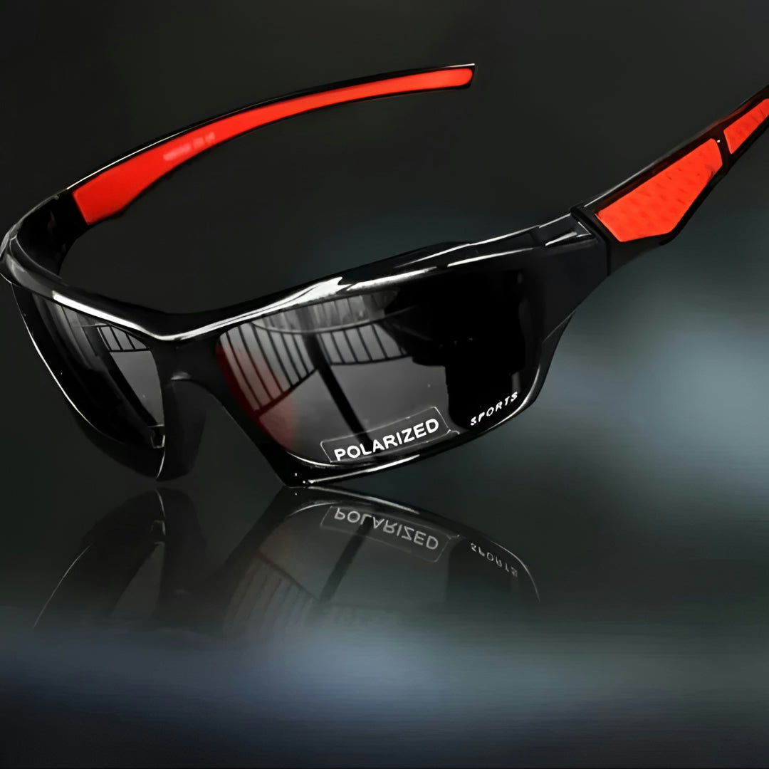 Sportsbrille med sorte, mørke glas og røde stænger, set skråt fra siden på mørk baggrund 1