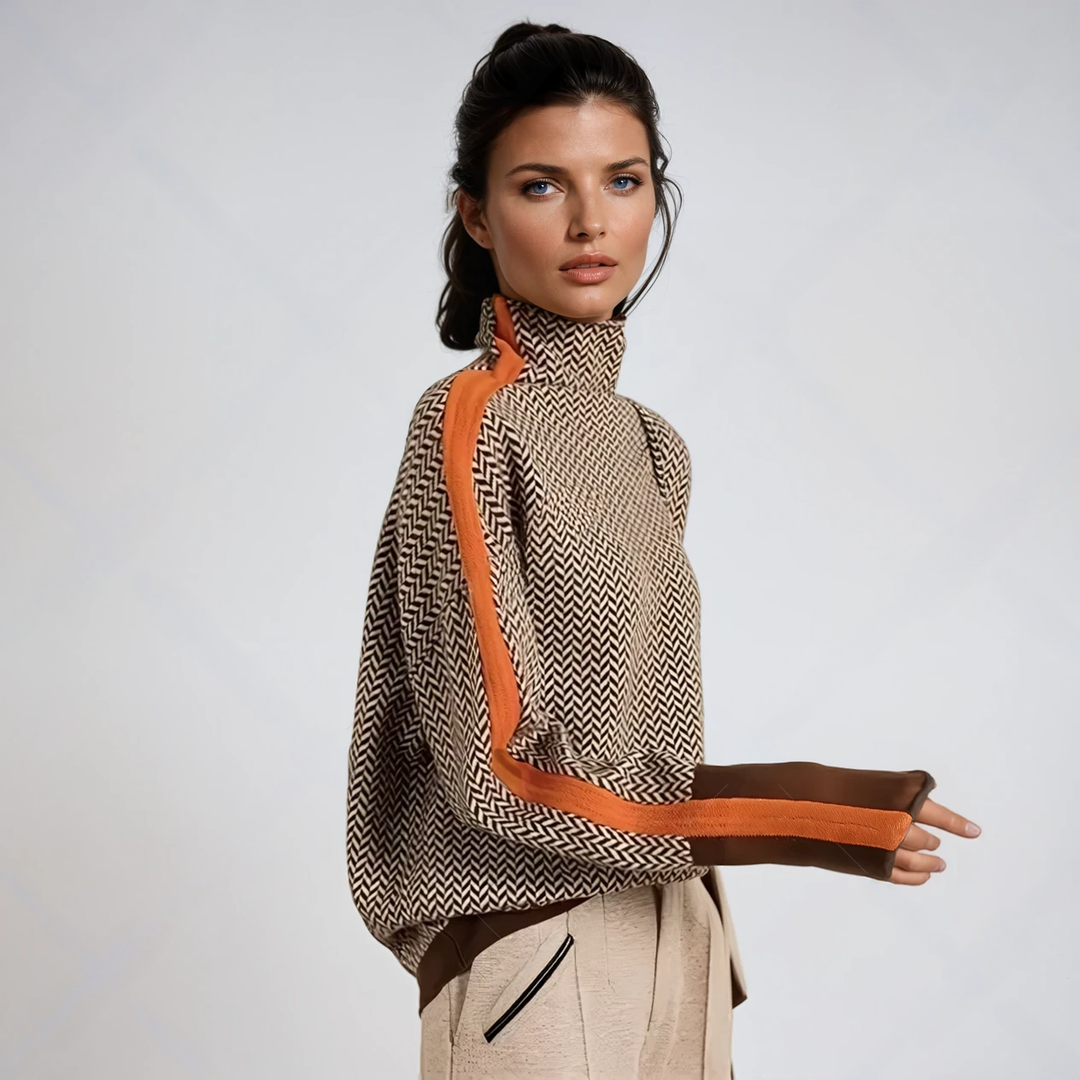 Model set fra siden i sweater med sildebensmønster, orange stribe langs ærmet, brune manchetter og lyse bukser. 1