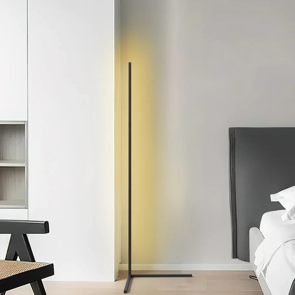 Sort gulvlampe med gulligt lys i et lyst rum med seng og en sort stol 7