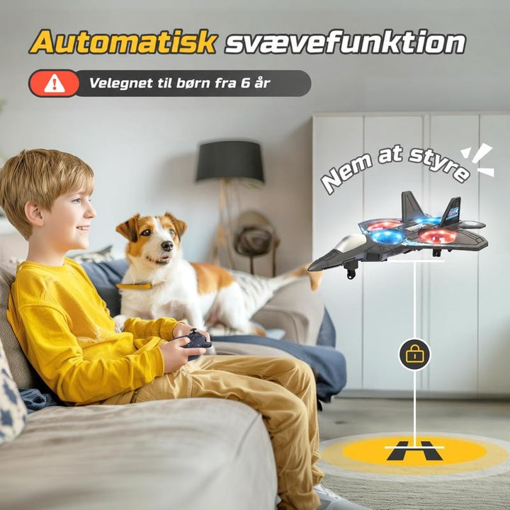 Dreng i gul trøje sidder i sofaen med fjernbetjening og styrer flyet, der svæver stille i stuen, mens en hund ser på. 6
