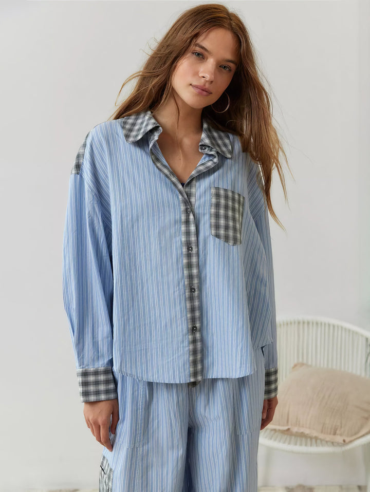 Model set forfra i blå stribet pyjamasskjorte med grå ternet krave, lomme og manchetter, siddende ved en hvid kurvestol med pude. 5