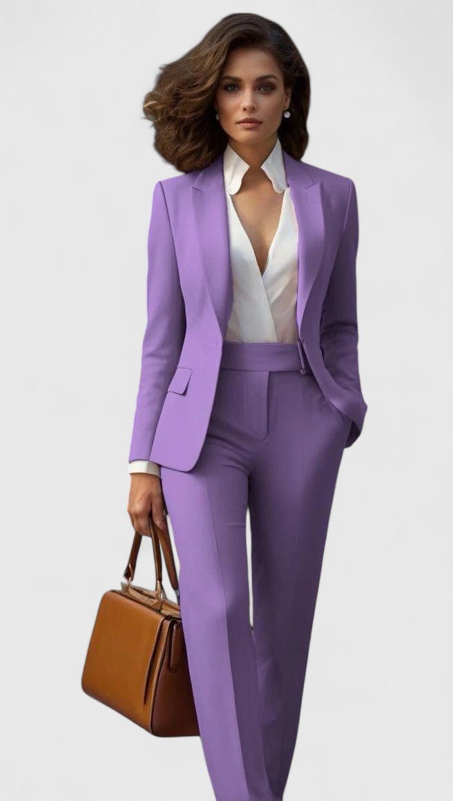 Model i lilla sæt med blazer og bukser med lige ben, hvid skjorte og brun håndtaske i hånden. 9