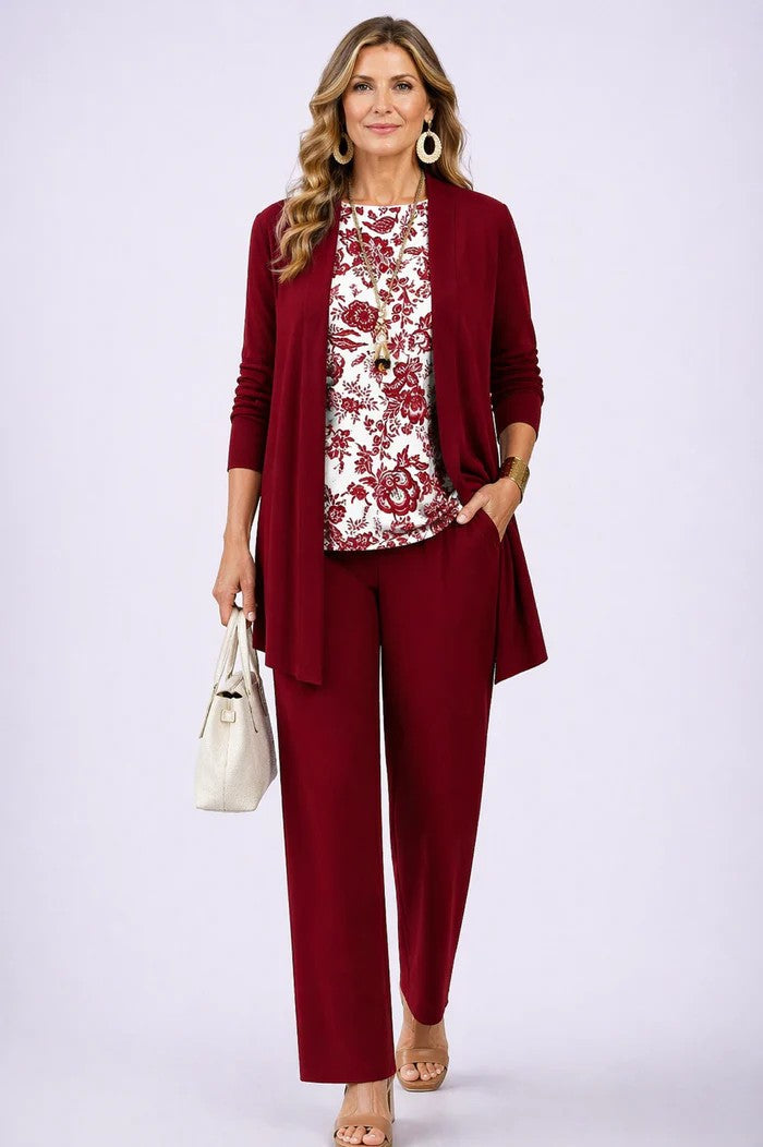 Model i vinrød cardigan og bukser med hvid top med rødt blomsterprint, set forfra med hånd i lommen. 13