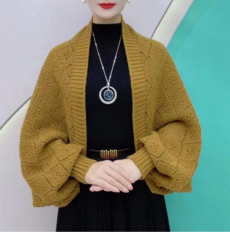 Model i sennepsgul strikket sjalcardigan med hulmønster og ribkant over sort top og plisseret nederdel 1