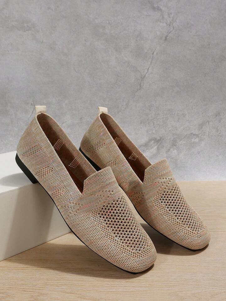 Beige strikkede slip-on sko stillet op ad en hvid kasse mod grå væg, med hulmønster og lille hælstrop. 7