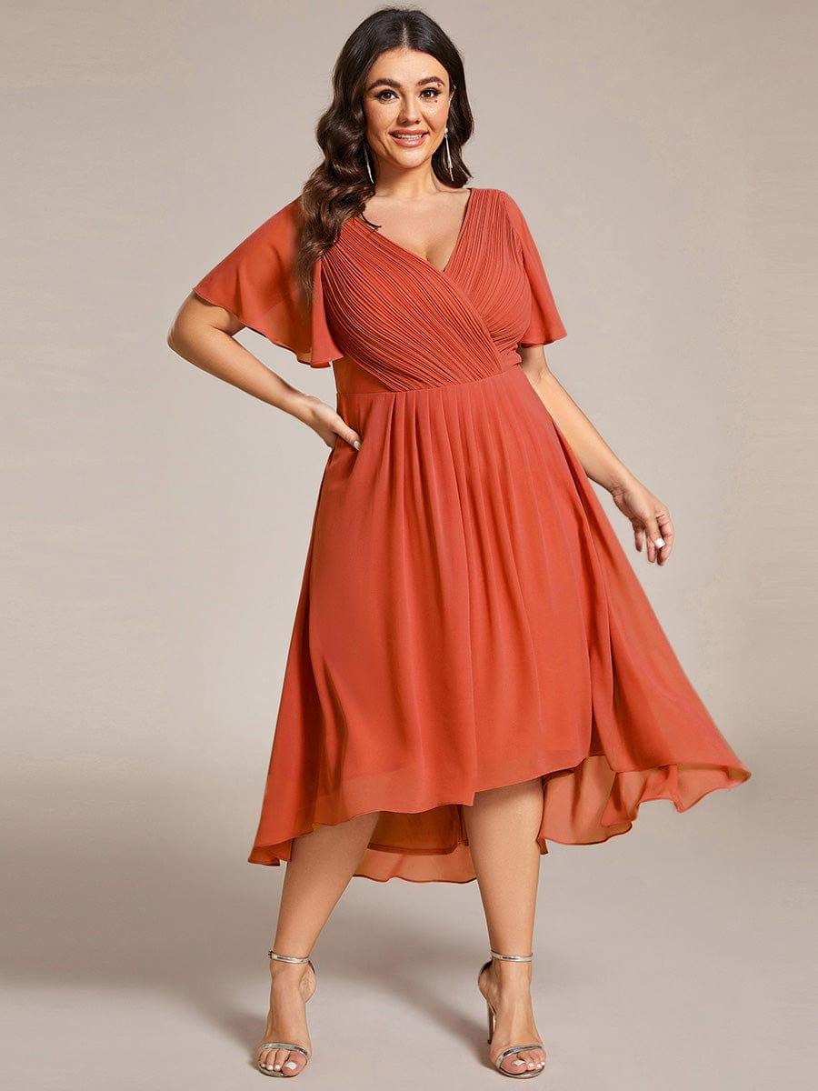 Plus size-model i rustorange chiffonkjole med plisseret V-hals, hånd på hoften og svingende nederdel. 97