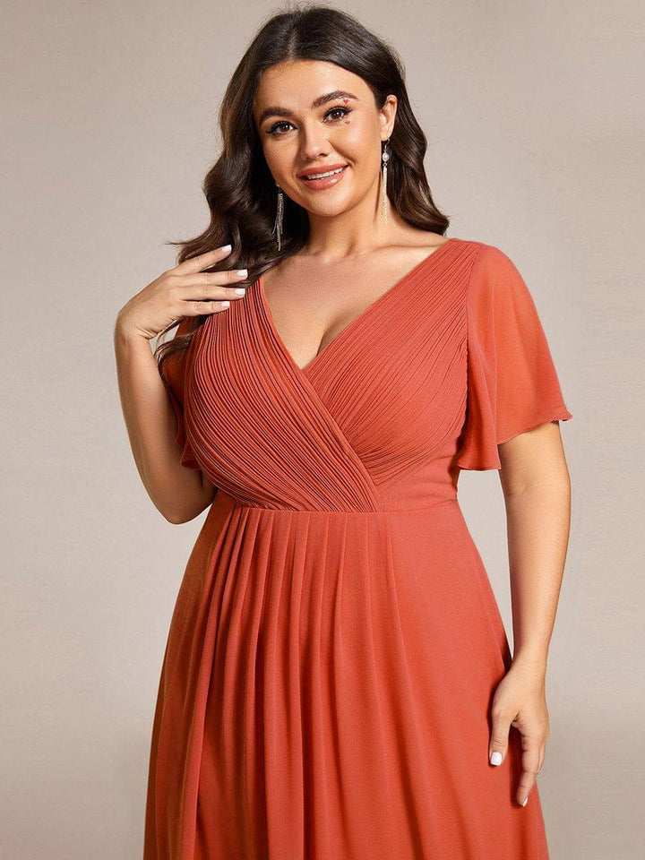 Nærbillede af rustorange kjoles plisserede overdel med V-hals og vingeærmer på smilende plus size-model. 99