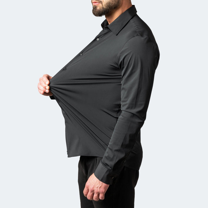 Sort skjorte set fra siden, hvor en model strækker stoffet langt ud foran maven for at vise skjortens elasticitet. 2