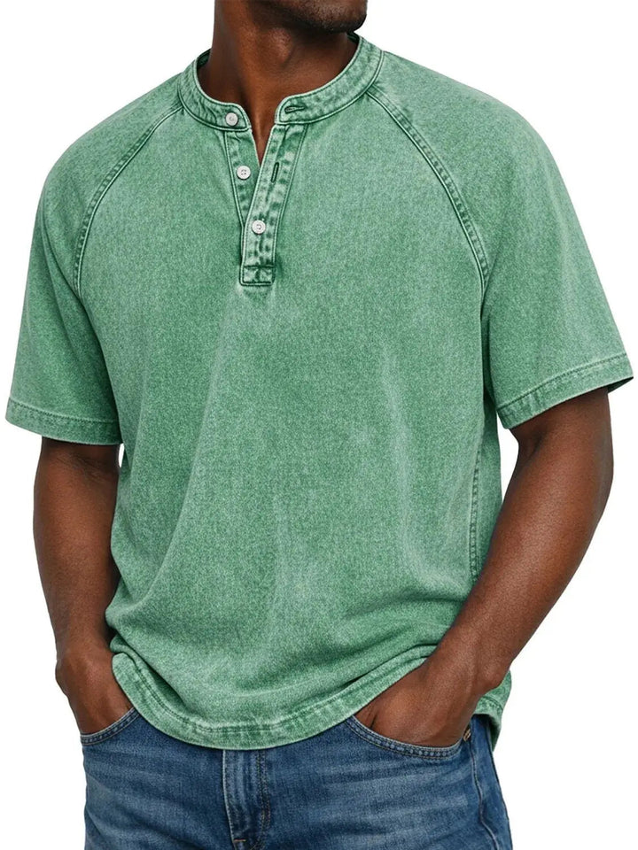 Mand i lysegrøn vasket Henley-T-shirt med raglanærmer og knaplukning, hænderne i lommerne på blå jeans. 6
