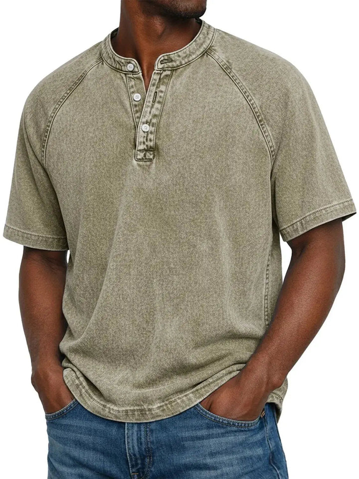 Mand i beige-grøn vasket Henley-T-shirt med raglanærmer og knapper i halsen, båret med blå jeans. 9