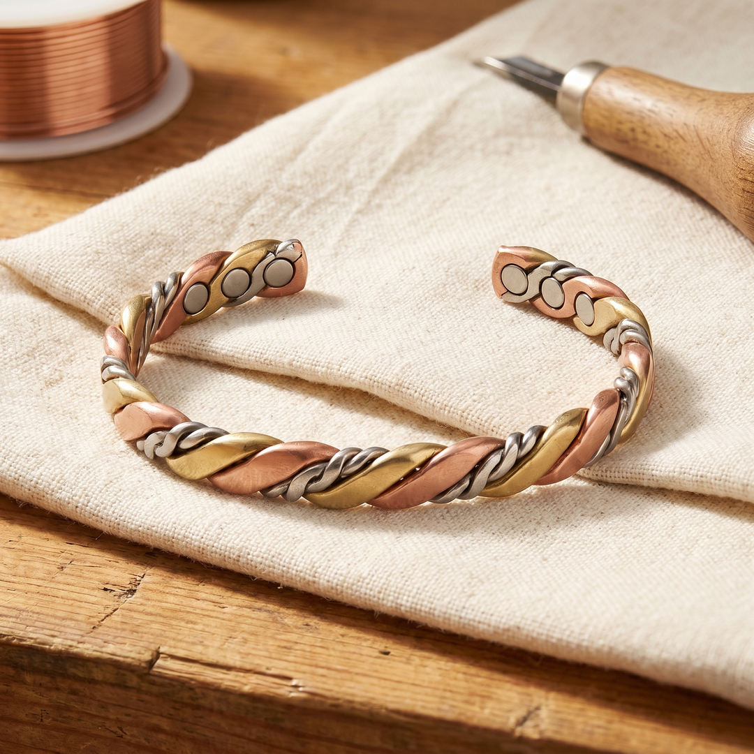 Snoet åbent armbånd i rosakobber, guldmessing og sølvfarvet metal med magneter, liggende på lærred 1