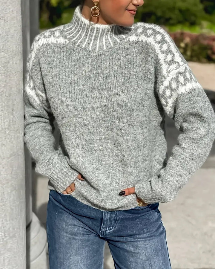 Grå strikket sweater med høj hals og hvidt mønster over skuldrene, båret af model med jeans udendørs. 5