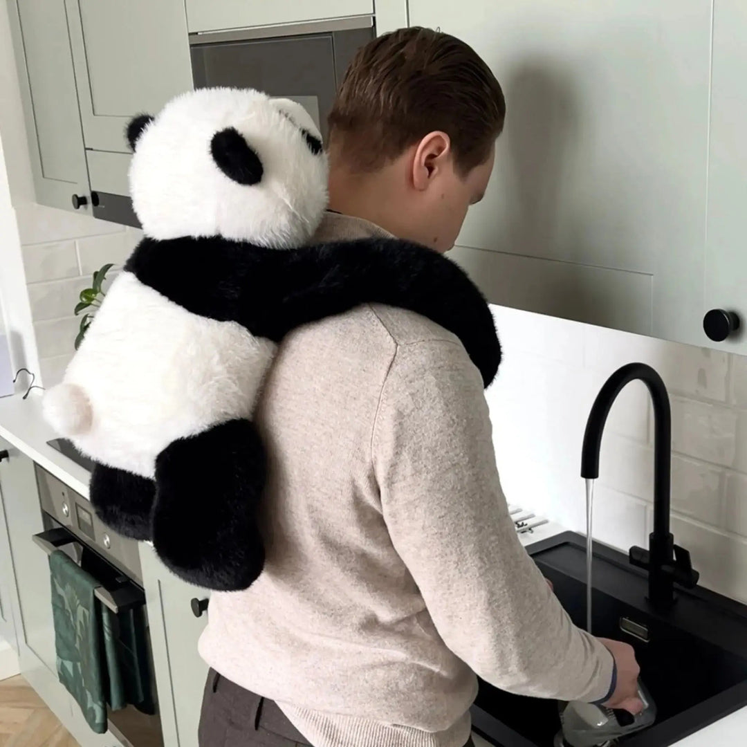 Mand står ved køkkenvasken og opvasker, mens panda-krammedyret hænger på hans ryg med armene om skuldrene. 10