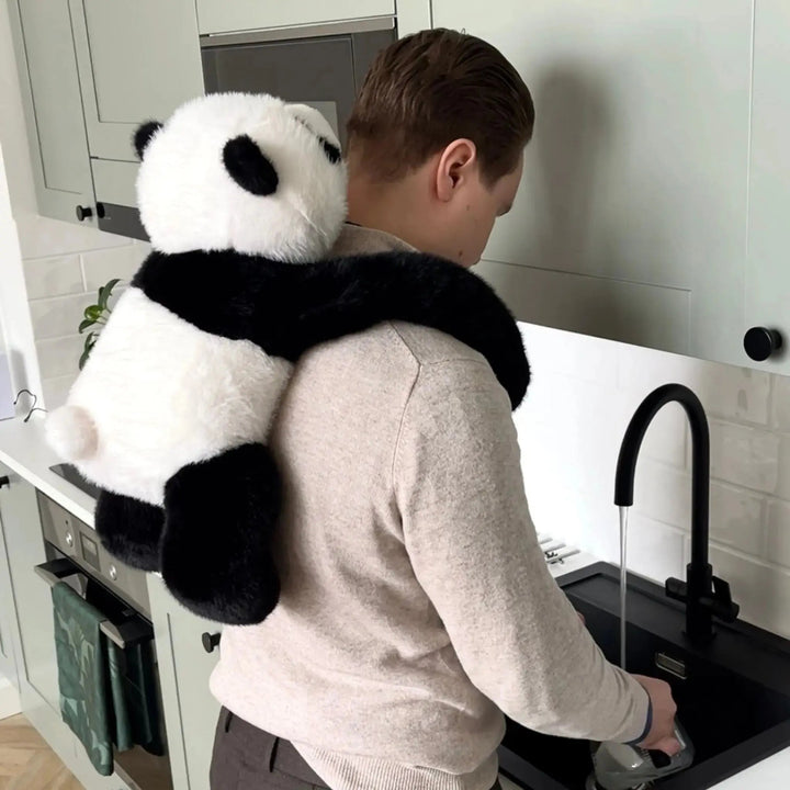 Mand står ved køkkenvasken og opvasker, mens panda-krammedyret hænger på hans ryg med armene om skuldrene. 10