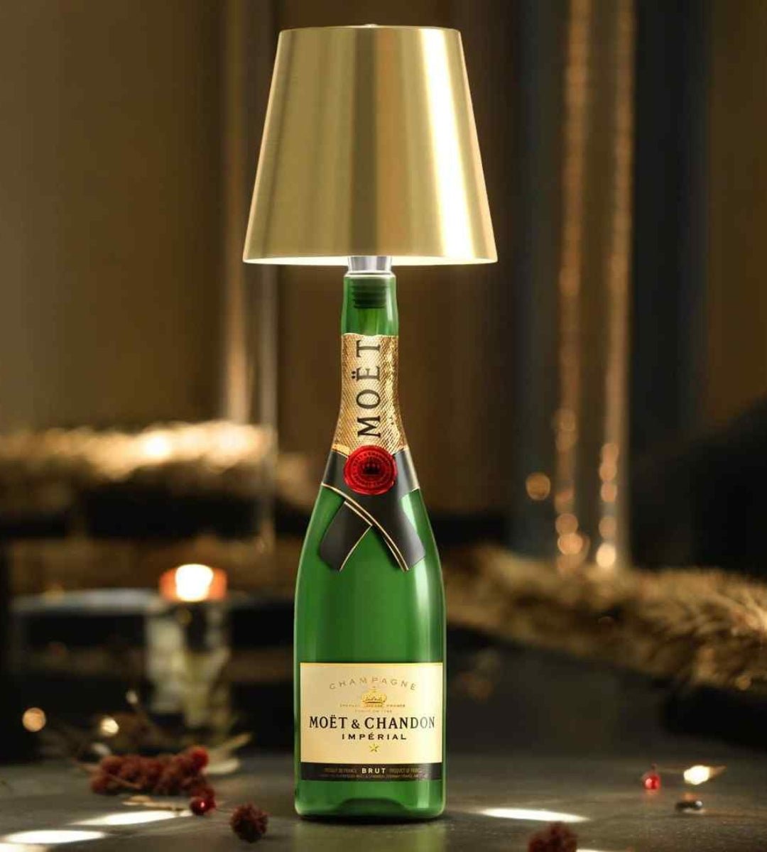 Guldfarvet lampeskærm sat i halsen på en grøn champagneflaske, der lyser blødt på et mørkt bord med festlig stemning. 1