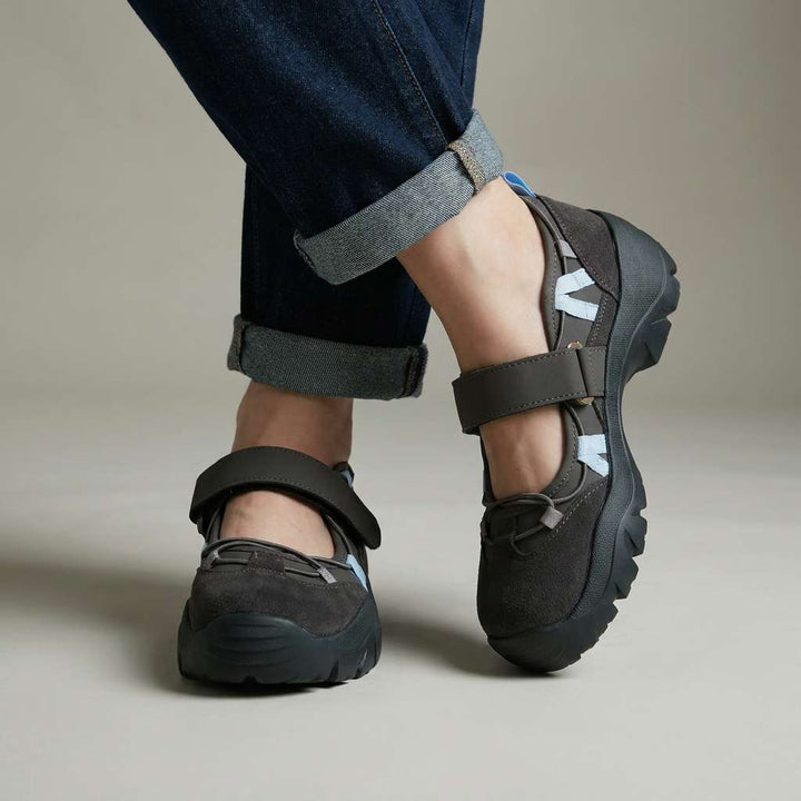 Mørkegrå sko med velcrostrop, lyseblå detaljer og kraftig sål, båret med oprullede jeans i studie. 2