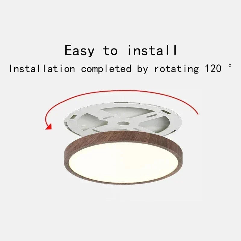 Loftlampen med mørk træfinish set skråt nedefra, med monteringsbeslaget løftet over lampen og en rød pil, der viser drejning ved montering. 1