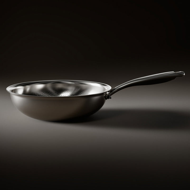 Wokpanden set fra siden med blank, afrundet skal og buet metalhåndtag, der viser den lave form og den flade bund. 2