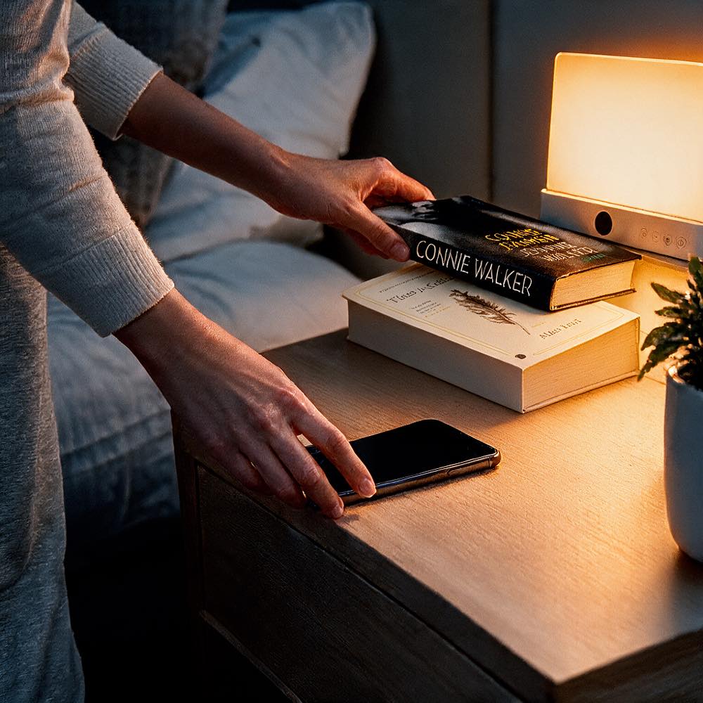 Kvinde lægger en bog og sin telefon på natbordet ved siden af den lysende lampe 10
