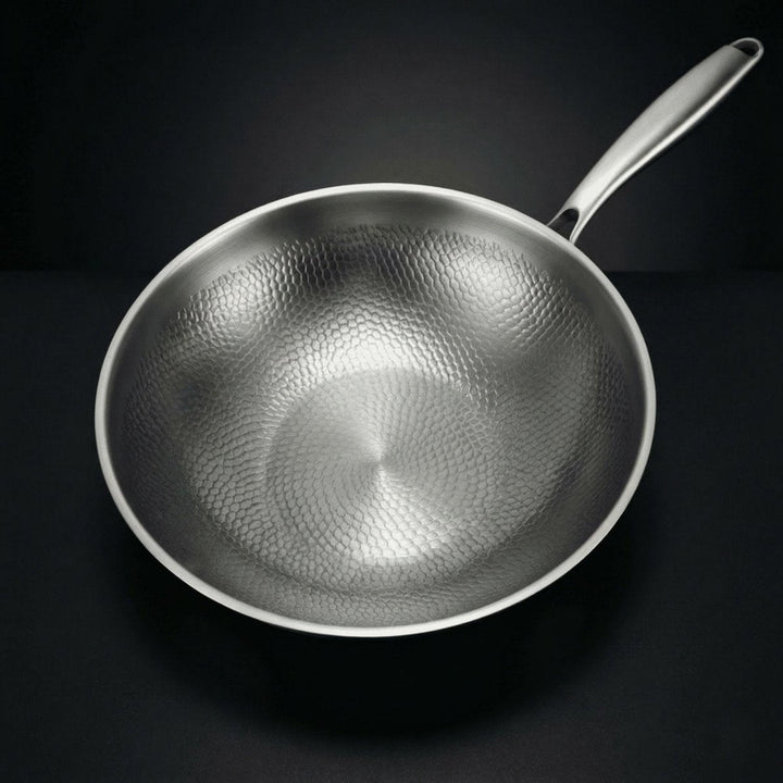 Wokpanden set ovenfra, så det hamrede mønster i bunden og på siderne træder tydeligt frem, med håndtaget til højre. 2