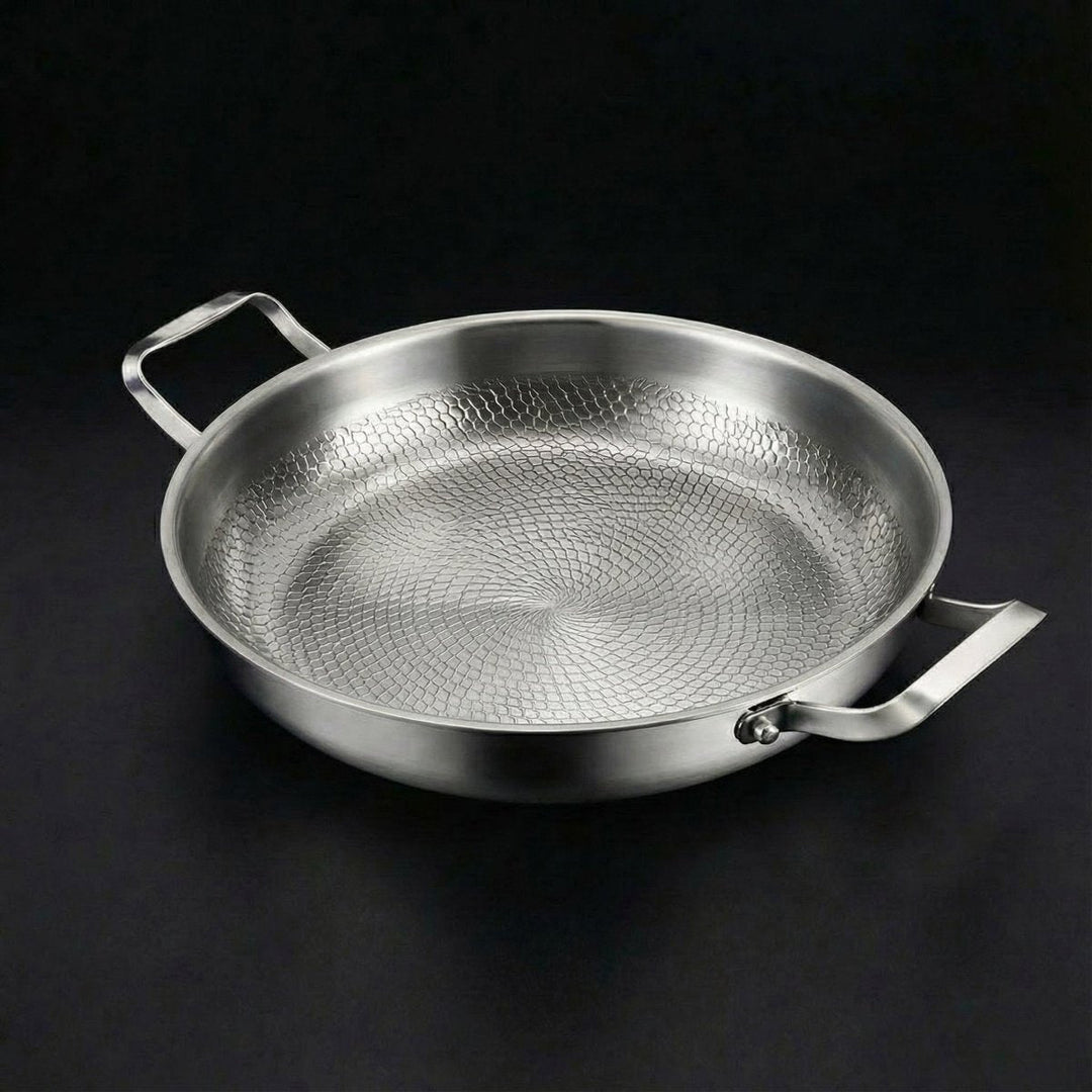 Tom pande set skråt ovenfra mod sort baggrund, med hamret mønster i bunden og to firkantede håndtag i børstet metal. 1