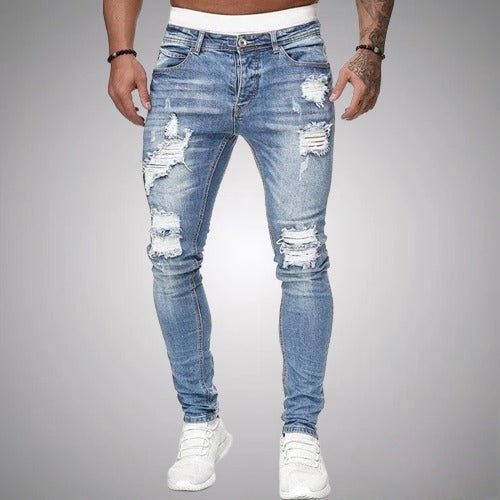Model i lyseblå slidte slim fit jeans med flossede huller på lår og knæ, set forfra med hvide sneakers. 2