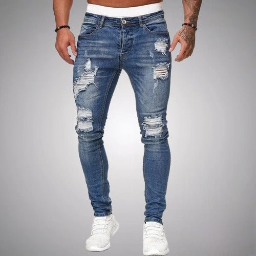 Model i mellemblå slidte slim fit jeans med flossede huller på lår og knæ, set forfra med hvide sneakers. 3