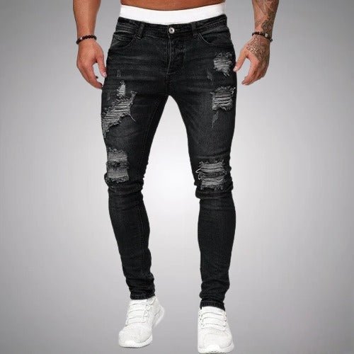 Model i sorte slidte slim fit jeans med flossede huller på lår og knæ, set forfra med hvide sneakers. 1