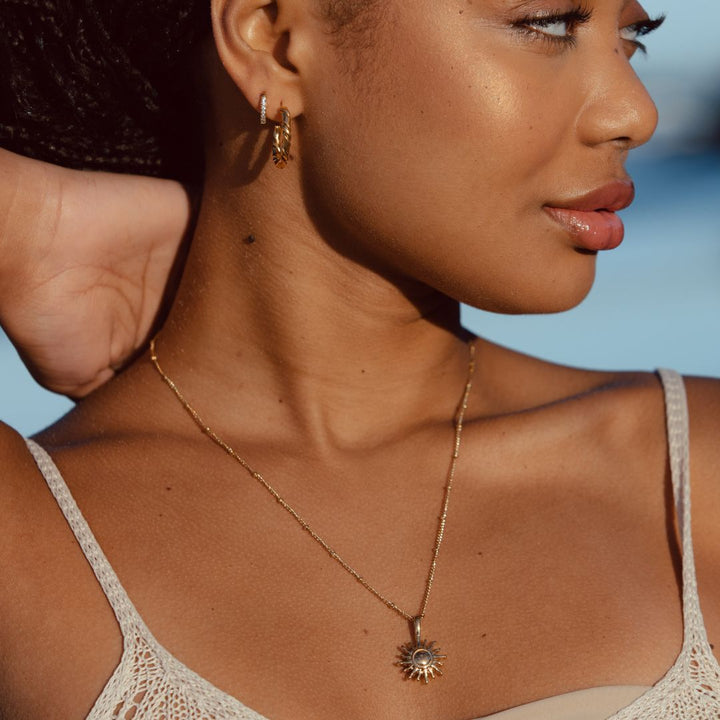 Frau mit goldener Sonnenanhänger-Halskette, eleganter Schmuck, modisches Accessoire.